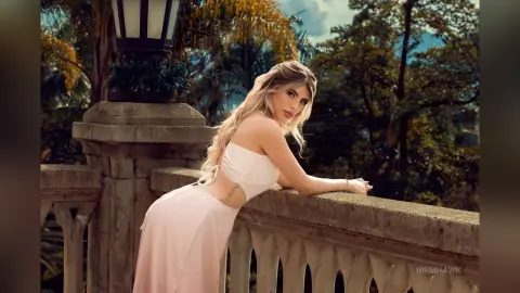 Elegant woman in a white strapless gown leaning on a stone balcony in a lush tropical garden setting.