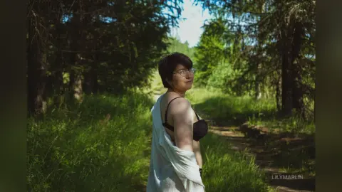 Young woman in a white cardigan posing in a sunny, lush green forest setting with a peaceful mood.