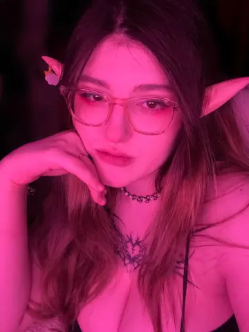 Young woman with elf ears and glasses posing in pink moody lighting wearing a black lace outfit.