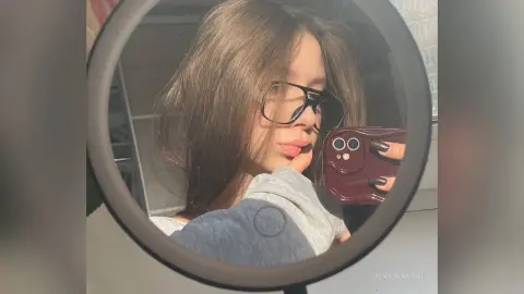 Young woman with glasses taking a casual mirror selfie in a bright room.