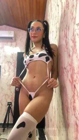 Woman in cow print bikini and white thigh-high stockings posing against a marble wall.