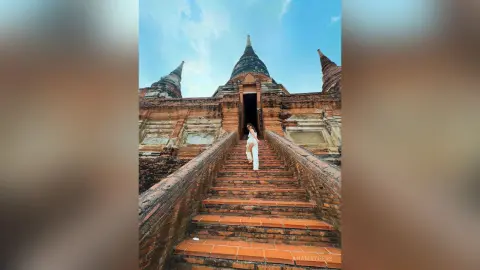 AnaMathers stands on a wide stone staircase in front of a large, ancient brick temple structure under a clear blue sky.