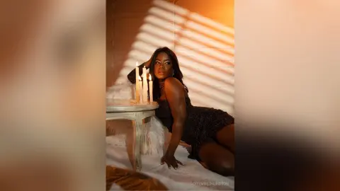 Elegant Black woman in a black sequin dress sitting by candlelight in a warm, moody indoor setting.