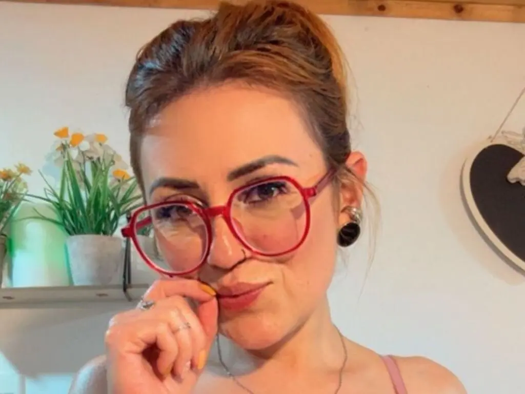Smiling woman with red glasses and messy bun in a bright indoor setting.