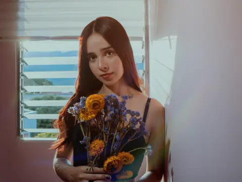 Young woman in a black tank top holding a bouquet of dried flowers by a sunny window with a soft, dreamy mood.