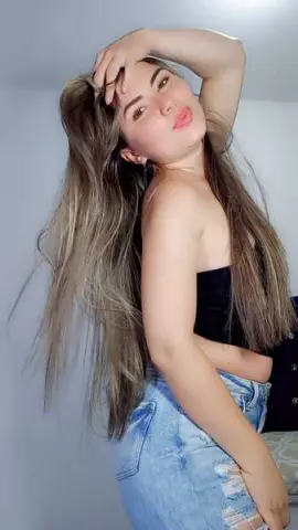 Young woman with long blonde hair wearing a black tube top and denim shorts in a bright indoor setting.