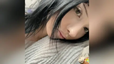 MarieJosePhilip looks into the camera with long black hair and a nose ring, wearing a white knit sweater.