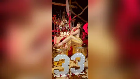Elegant woman in a gold dress sitting by a celebratory 33rd birthday display with gold decor and warm lighting.
