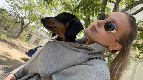 BonnyWalace poses outdoors in sunglasses while holding a small black and brown puppy near her face.
