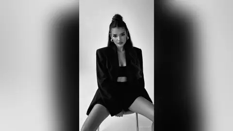 Elegant woman in a black blazer and shorts posing in a minimalist studio setting, black and white portrait.