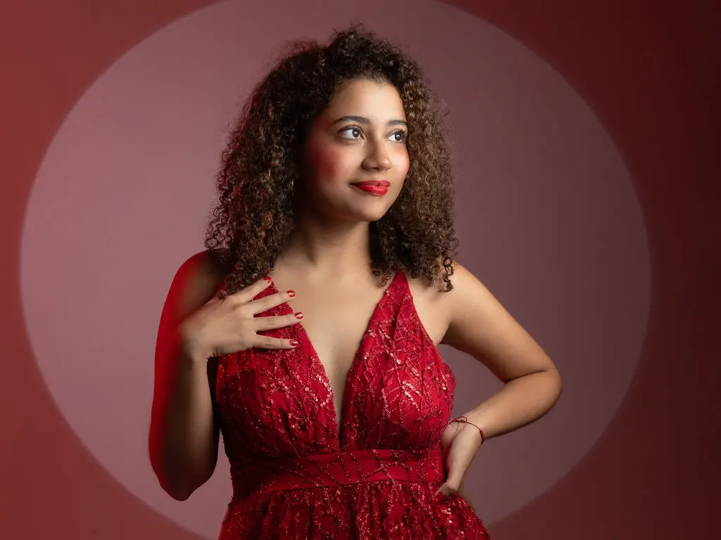 EmmaHarper wears a red lace plunging neckline dress while posing against a circular red spotlight.