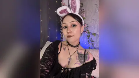Woman with bunny ears and black lace outfit posing in a room with fairy lights and a moody aesthetic.