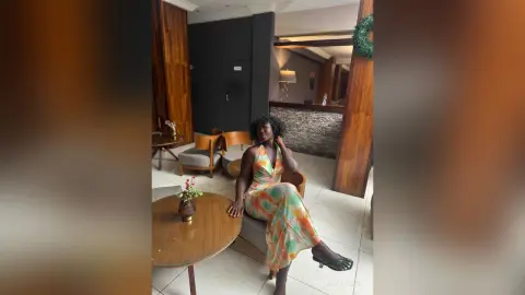 Elegant woman in a colorful floral maxi dress sitting in a modern, moody lounge setting.