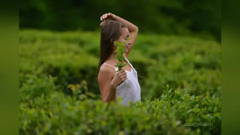 Young woman in a white tank top holding a green fern in a lush, serene green field.