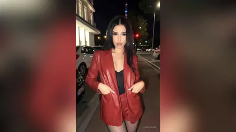 Stylish woman in a red leather blazer and shorts standing on a city street at night.