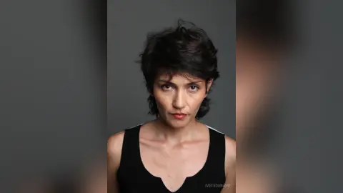 IveteDurand looks directly at the camera with short dark hair, wearing a black tank top against a plain grey background.