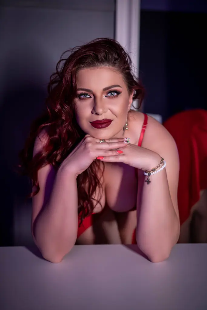 QueenNatashaX poses on a light floor, wearing a black lace bra and showing her red hair and bare skin.