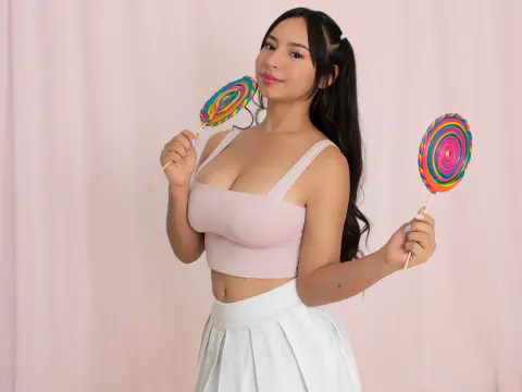 Young woman in a pink crop top and white skirt holding colorful swirl lollipops against a pink backdrop.