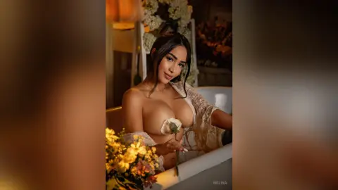Beautiful woman in a white lace robe relaxing in a bathtub surrounded by flowers in a romantic setting.
