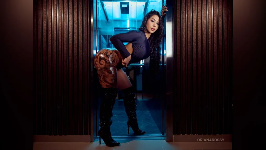 OrianaRossy β OrianaRossy poses in a doorway wearing a tight blue top, patterned brown shorts, and tall black boots.