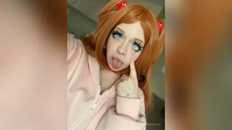 Cosplayer with bright blue eyes and orange hair in a pink hoodie making a playful expression.