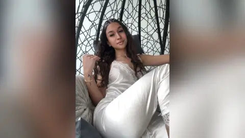 Young woman in white satin pajamas relaxing in a hanging egg chair with a peaceful mood.