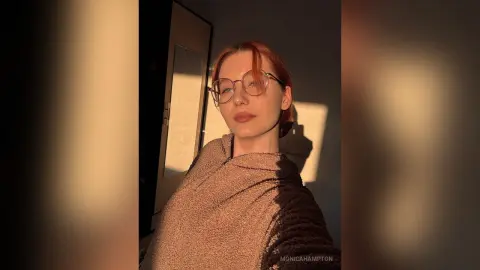 Redheaded woman in glasses wearing a cozy textured sweater in warm sunset lighting.