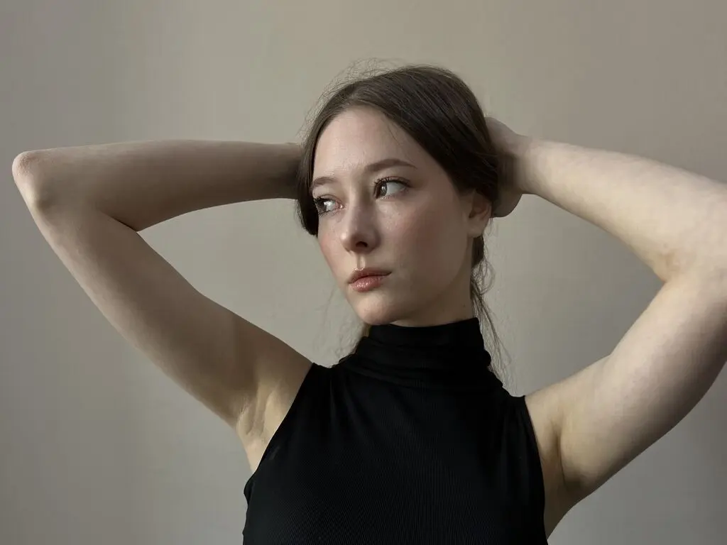 Young woman in a black sleeveless turtleneck posing thoughtfully against a neutral studio background.