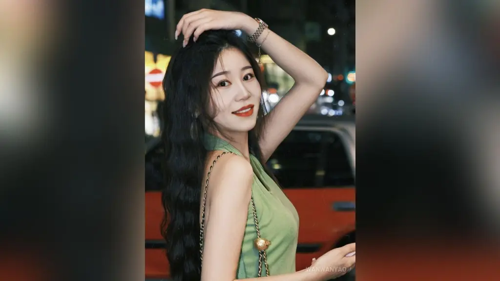 WanwanYao — Elegant woman in a green sleeveless top posing with long wavy hair in a nighttime city street setting.