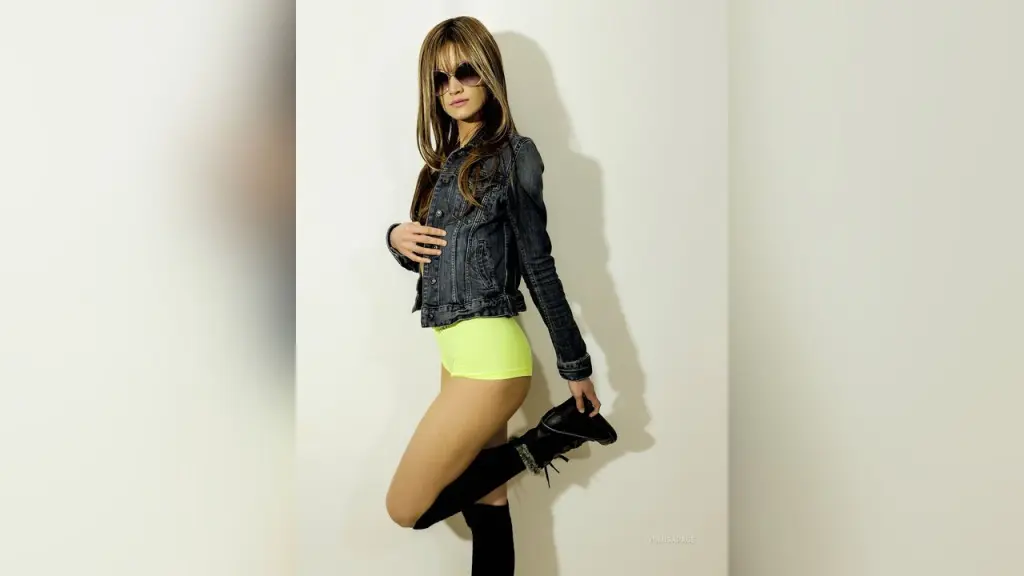 YumisaPage — Stylish woman in a denim jacket and neon yellow shorts posing confidently against a white wall.