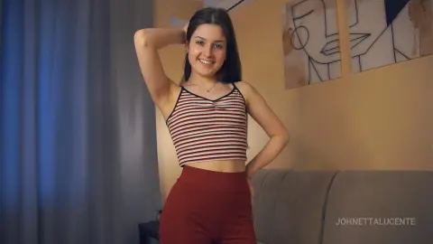 Smiling young woman in a striped crop top and red leggings posing in a cozy living room.