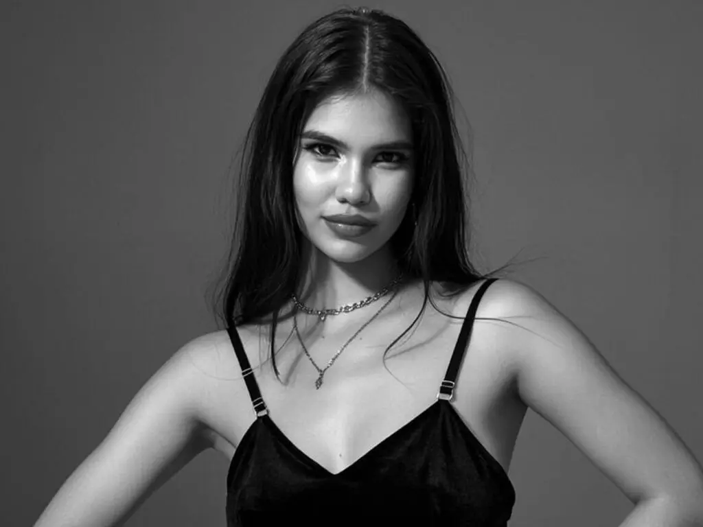 Portrait of a young woman in a black camisole and silver necklaces against a dark studio background.