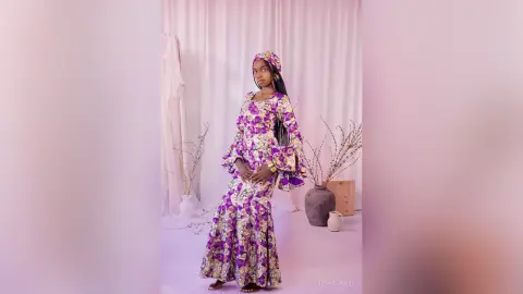 Elegant woman in a purple floral maxi dress and matching headwrap posing in a bright, minimalist studio.