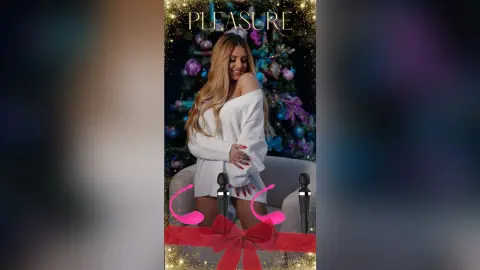 Anita poses in a white off-the-shoulder sweater against a dark, decorated holiday tree background.