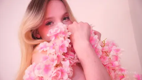 Blonde woman wrapped in pink cherry blossom flowers against a soft pink background for a romantic aesthetic.