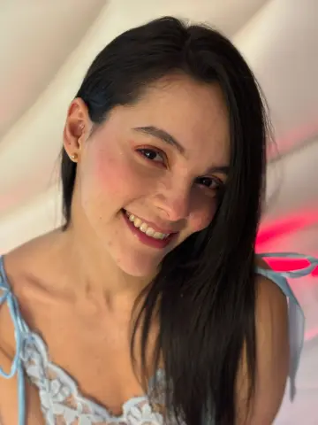 Smiling young woman with long dark hair wearing a light blue lace camisole in a bright, airy setting.