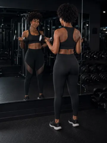 KylieDecks — KylieDecks stands in a gym mirror wearing black sports bra and leggings while holding dumbbells.