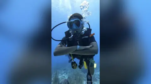 Female scuba diver in black gear swimming underwater in clear blue ocean water with bubbles.