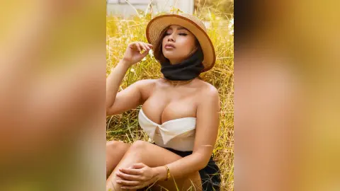 Beautiful woman in a white top and straw hat relaxing in a sunny golden field.