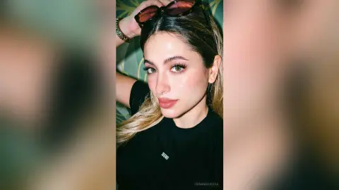 IrinaMolkova poses with sunglasses on her head, wearing a black t-shirt and looking directly at the camera with long blonde hair.