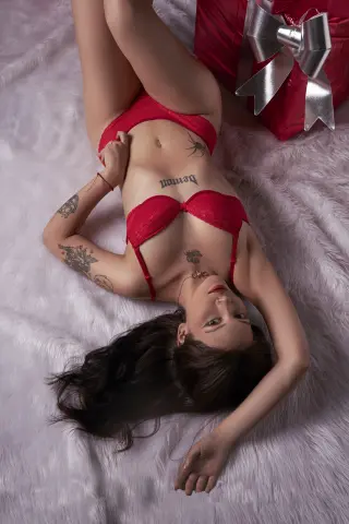 Woman in red lace lingerie lying on white faux fur next to a large red gift box in a romantic mood.