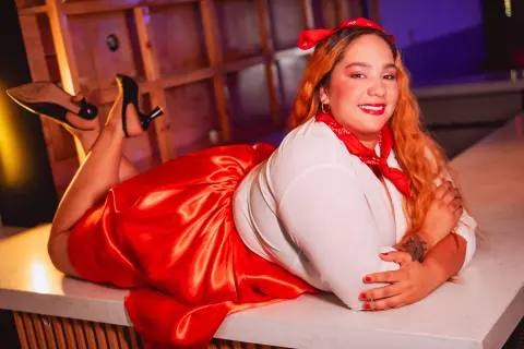 Smiling woman in vintage red skirt and white blouse reclining on a marble counter in a warm, retro setting.