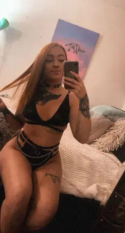 Young woman with long red hair wearing black lingerie and posing in a cozy bedroom setting.