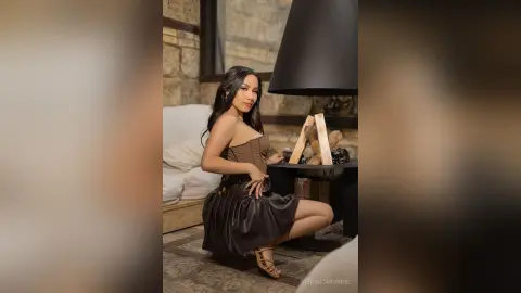 Elegant woman in a brown strapless cocktail dress posing in a cozy, rustic living room setting.
