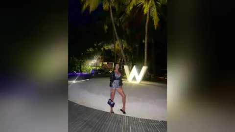 Stylish woman in a patterned mini dress and black leather jacket posing by a glowing W hotel sign at night.