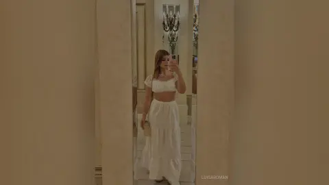 Elegant woman in a white puff-sleeve crop top and maxi skirt posing in a luxury mirrored hallway.
