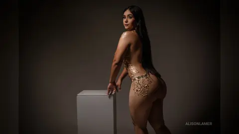 Curvy woman in gold body jewelry posing elegantly against a dark studio background.