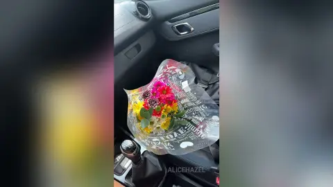 Colorful bouquet of fresh spring flowers in a clear gift wrap sitting on a black car passenger seat.