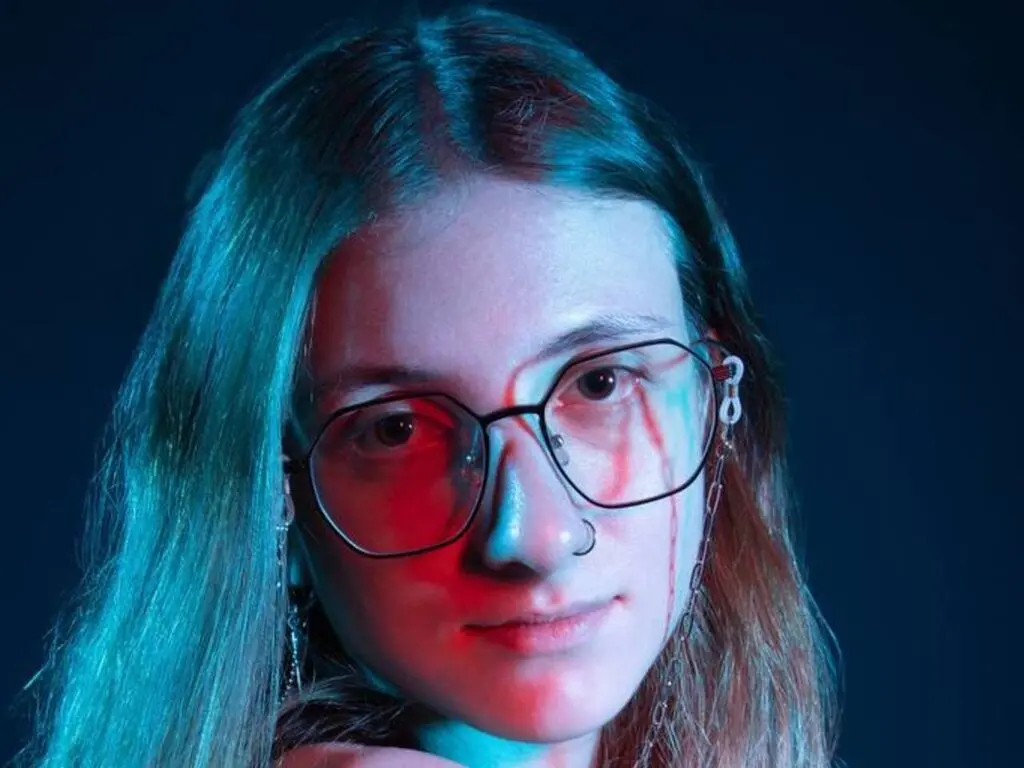 Young woman with glasses and long hair in moody blue and red neon lighting.