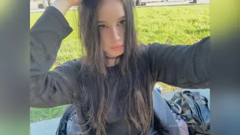 MarvellaRovella poses outdoors in a black long-sleeve shirt with her long dark hair falling over her face.